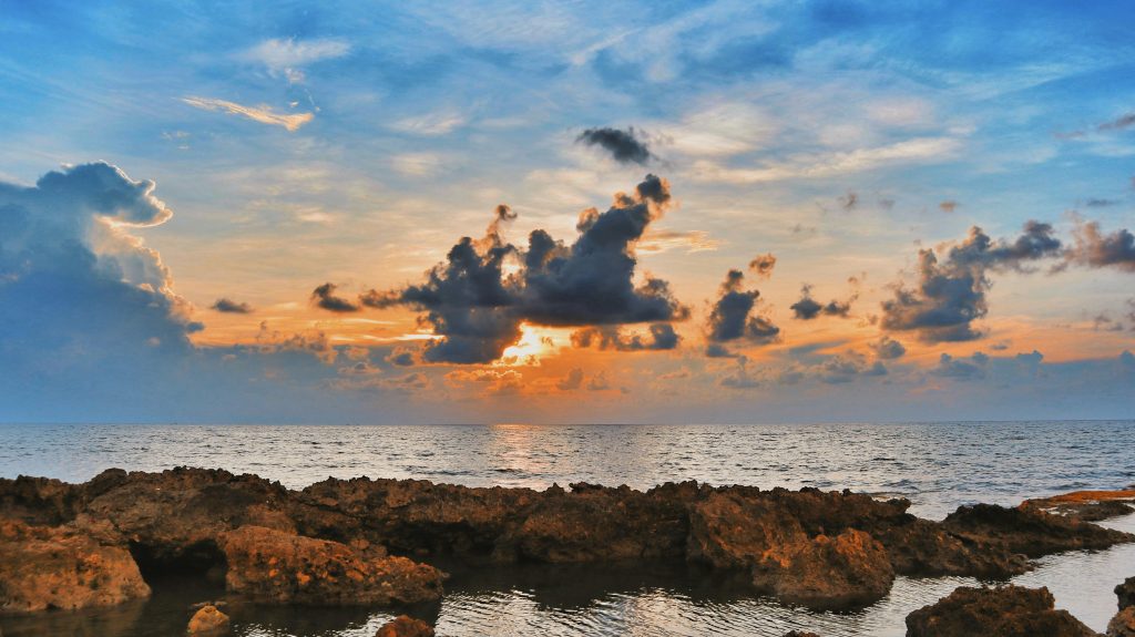 Rocky shoreline at sunset in La Union, with tide pools and dramatic clouds over the sea.