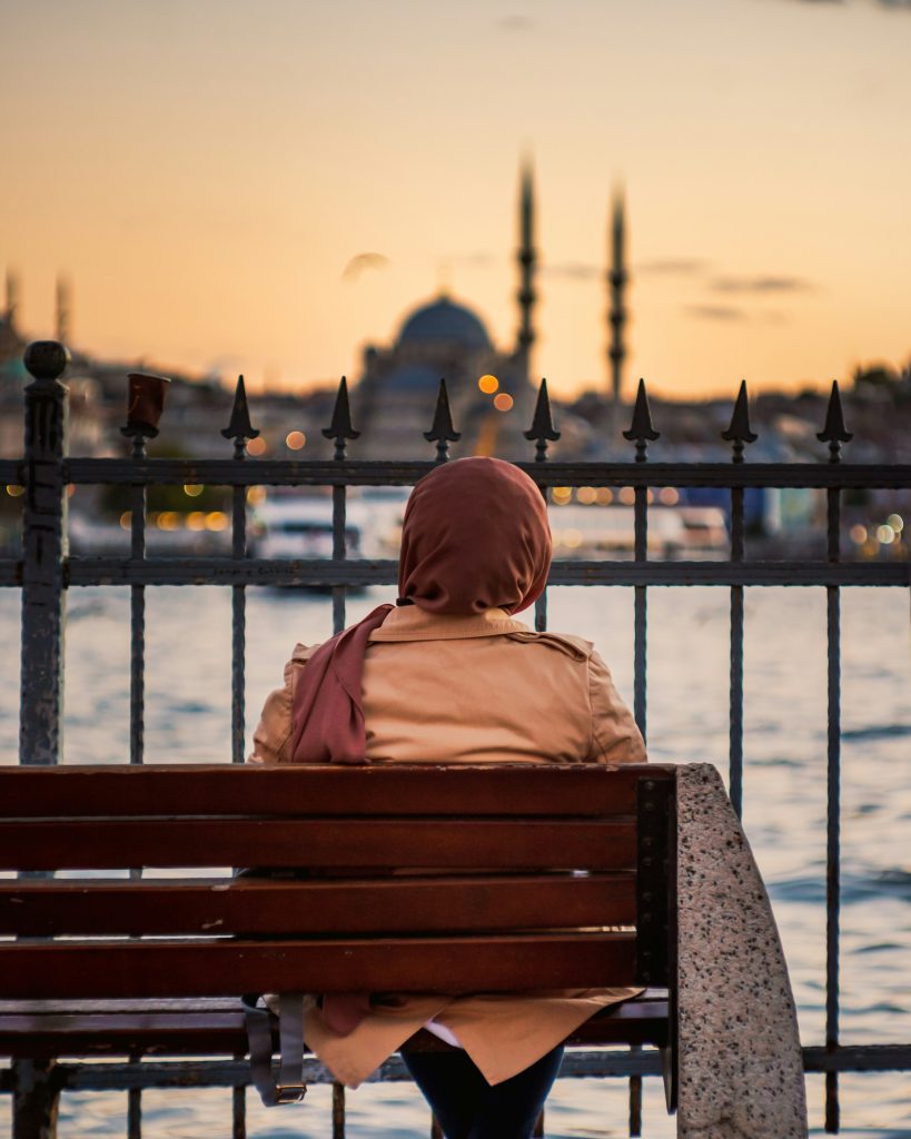 Person sitting by waterfront at sunset with mosque skyline in background