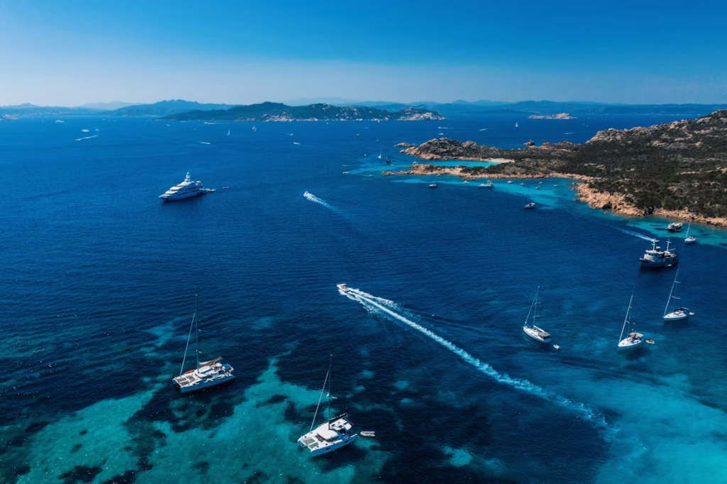 Boats and yachts navigating clear blue waters near a Mediterranean island coastline
