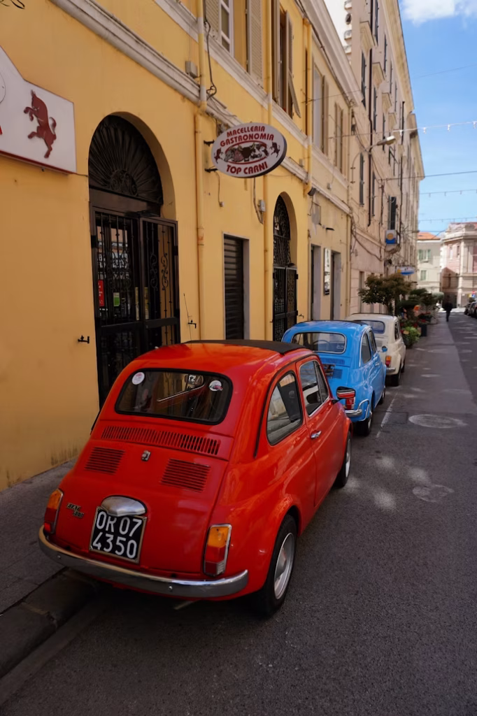 Small vintage cars parked along a narrow street in an Italian town