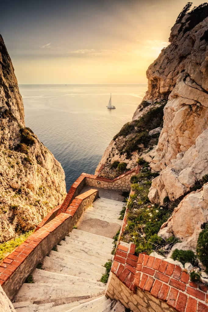 Stone staircase descending between cliffs toward the Mediterranean Sea at sunset